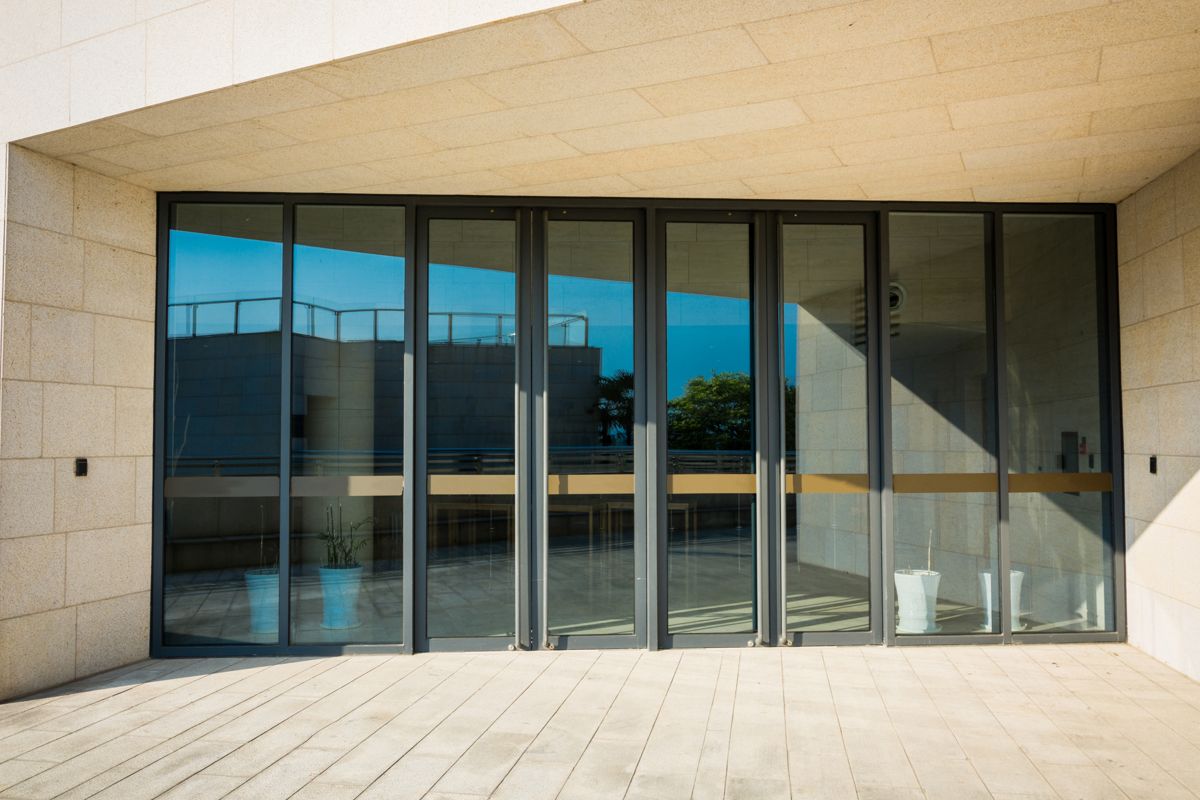 Entrée de bâtiment entièrement vitrée, avec de grandes baies et des portes en verre sur un sol clair